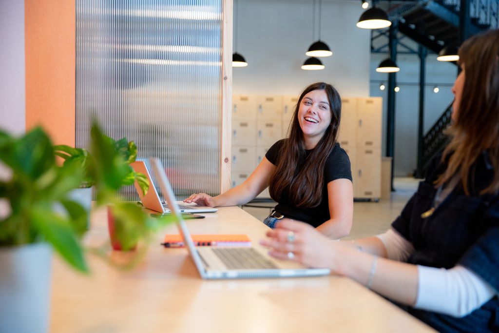two women talking and laughing whilst working at a shared co-working desk