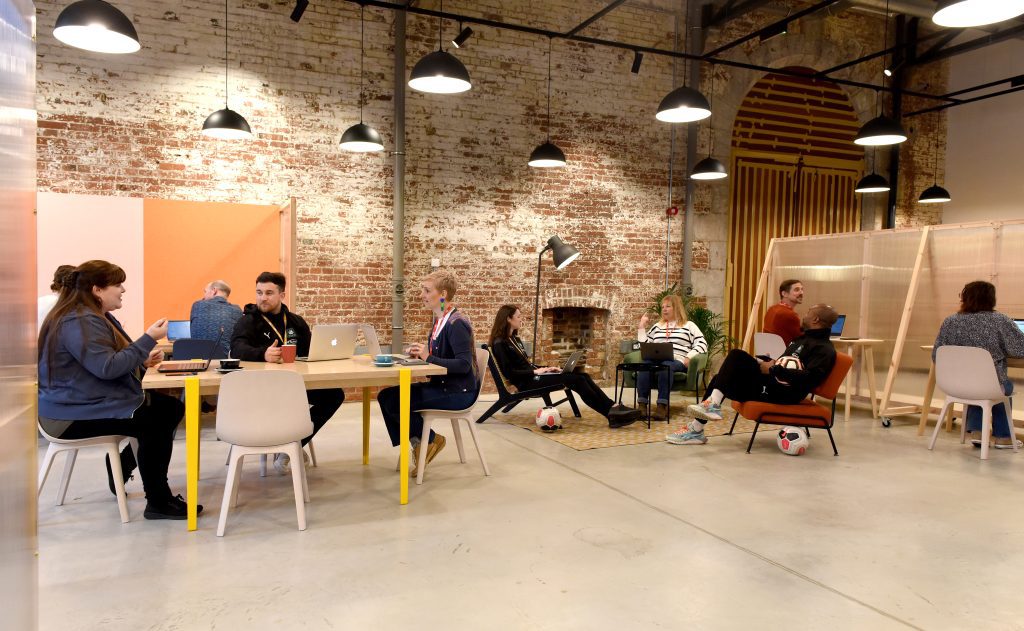 Group of people sat at a range of different seating, hot desking in a shared co-working space